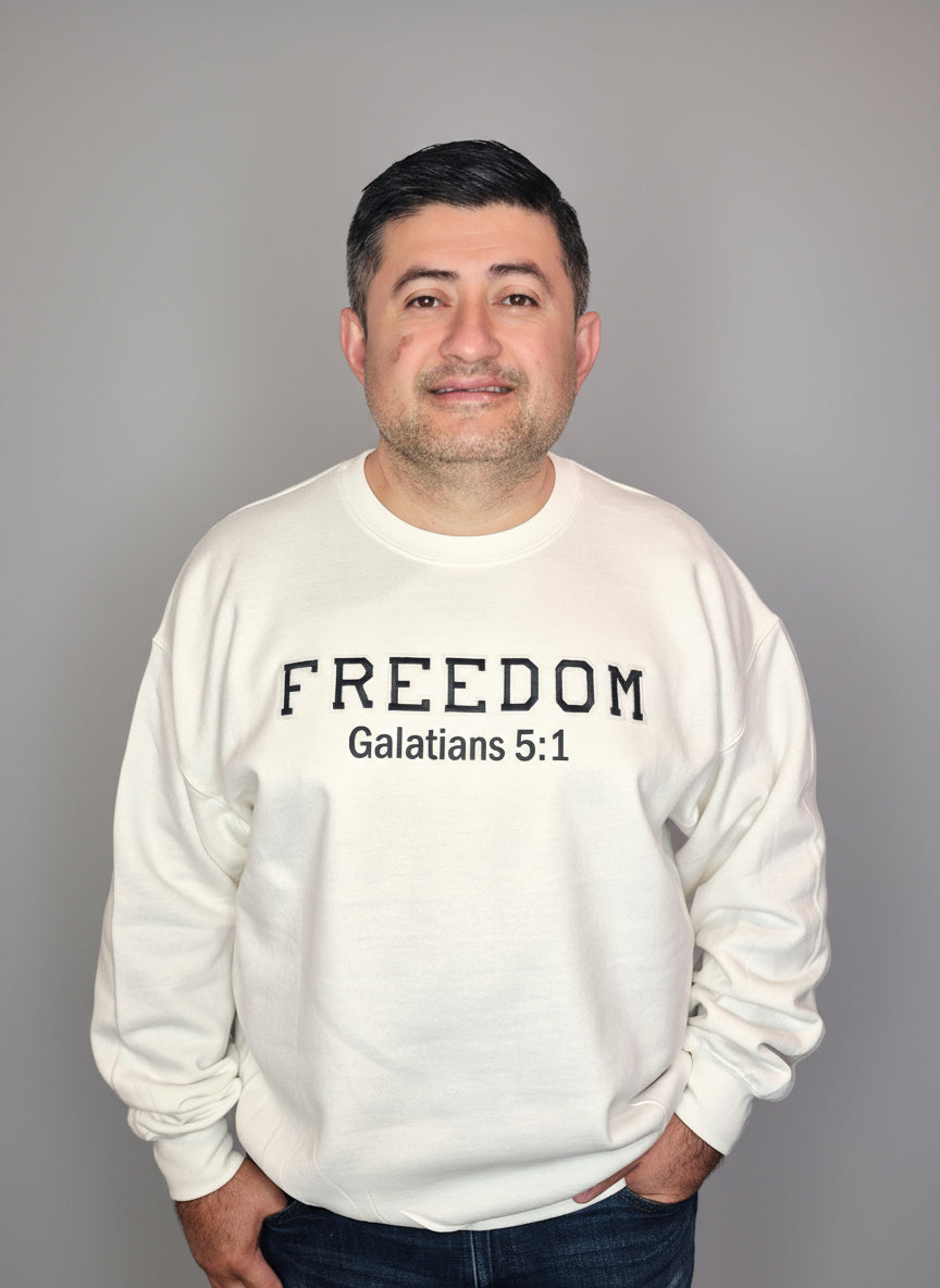Person wearing a white sweatshirt with 'FREEDOM Galatians 5:1' text standing in front of a white door.