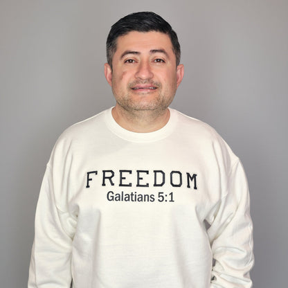 Person wearing a white sweatshirt with 'FREEDOM Galatians 5:1' text standing in front of a white door.
